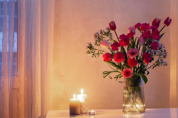 Flores rosas en jarrón moderno de vidrio con velas encendidas en interior blanco