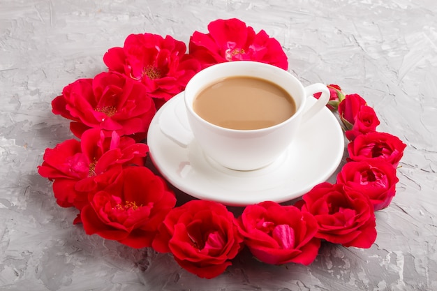 Flores de rosas rojas en espiral y una taza de café sobre concreto gris