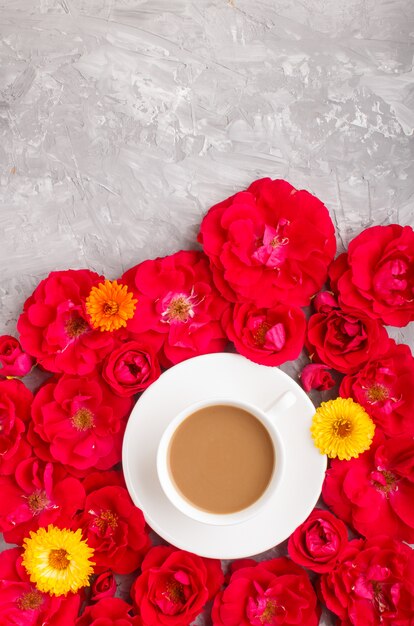Flores rosas rojas y una taza de café en concreto gris
