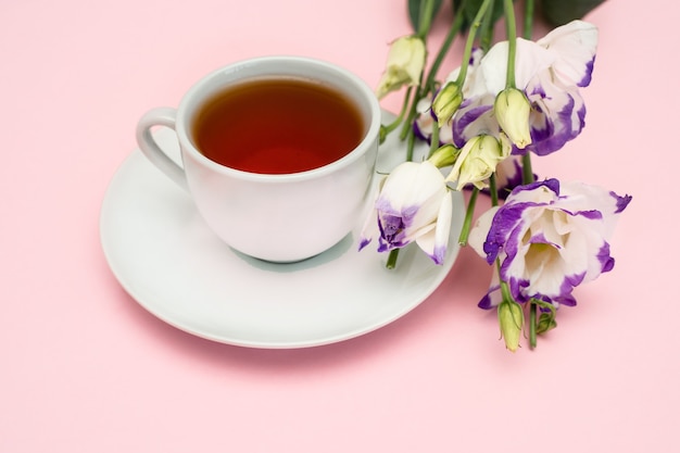 Flores roxas e uma xícara de café branca em um fundo rosa. um lindo banner com espaço para copiar.