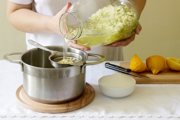 Flores de saúco, agua, limón y azúcar, ingredientes y una mujer preparando un jarabe de saúco. Estilo rústico