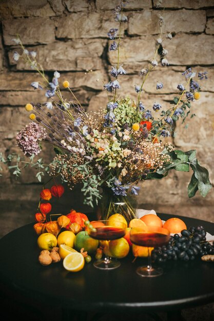 Flores secas en jarrón en la mesa con frutas y vino tinto