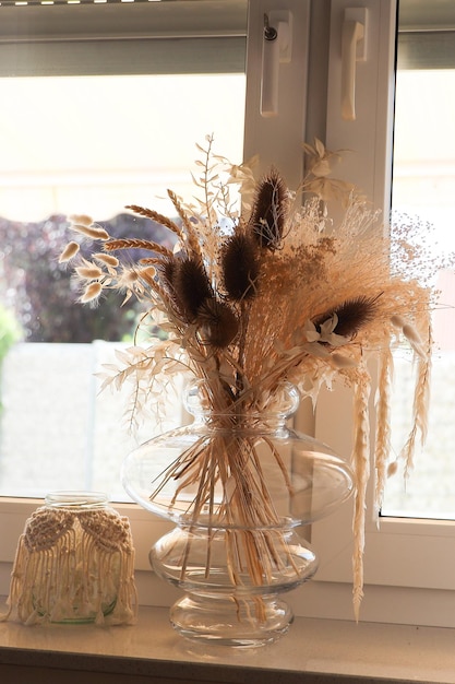 flores secas y paja en un jarrón transparente en el alféizar de la ventana