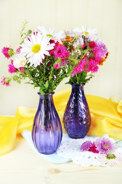 Flores silvestres em vasos de vidro na mesa sobre fundo claro