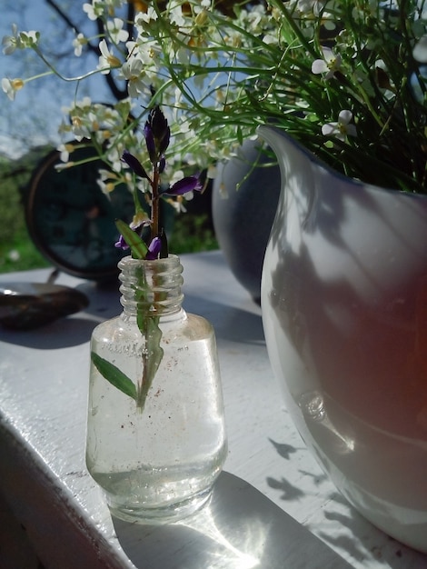 Flores silvestres frescas en jarra de porcelana reloj antiguo silla de madera blanca hierba verde y cielo azul