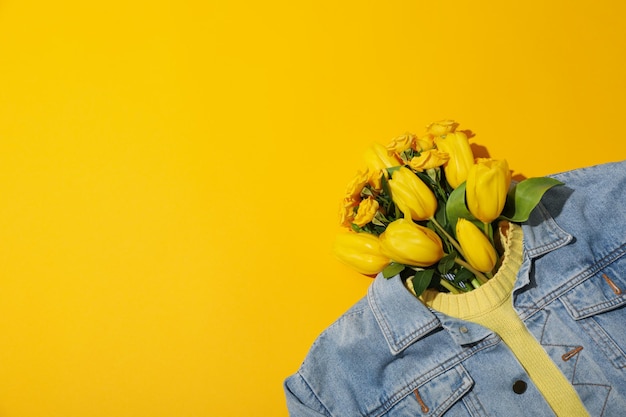 Flores en suéter y chaqueta de vaqueros en espacio de fondo amarillo para el texto