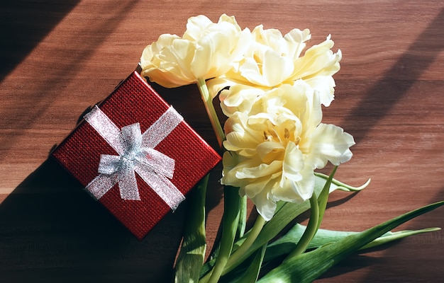 Flores de tulipán amarillo con caja de regalo roja sobre la mesa.