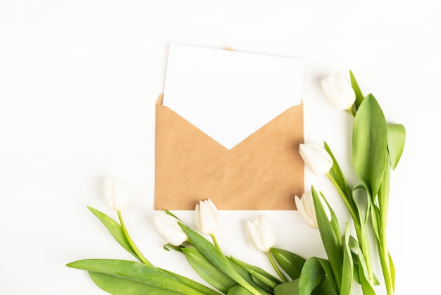 Flores de tulipán blanco recién cortado y tarjeta en blanco con vista superior de sobre sobre fondo blanco.