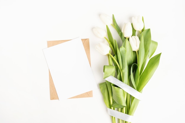 Flores de tulipán blanco recién cortado y tarjeta en blanco con vista superior de sobre sobre fondo blanco.