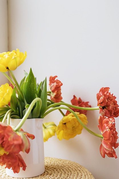 Flores de tulipán florecientes rojas amarillas desenfocadas con tallos verdes y hojas en una jarra de cerámica blanca sobre fondo de pared blanca clara Papel tapiz de botánica floral creativa Tarjeta de felicitación creativa mínima