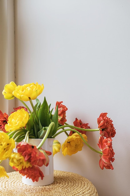 Flores de tulipán florecientes rojas amarillas desenfocadas con tallos verdes y hojas en una jarra de cerámica blanca sobre fondo de pared blanca clara Papel tapiz de botánica floral creativa Tarjeta de felicitación creativa mínima