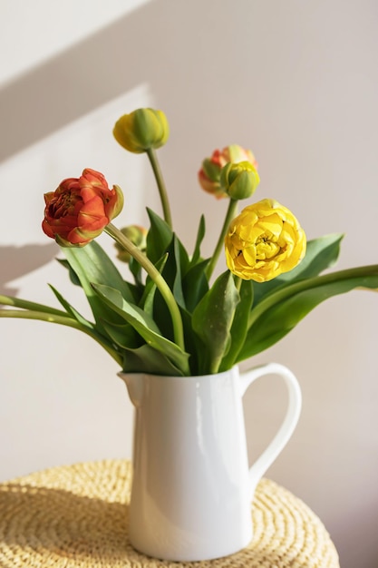 Flores de tulipán rojo amarillo con tallos verdes y hojas en una jarra de cerámica blanca sobre una pared blanca de sombra clara y fondo de ventana Papel tapiz de botánica floral creativa Tarjeta de felicitación creativa mínima