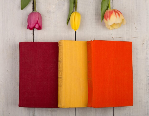 Flores tulipanes y libros de colores sobre una mesa de madera blanca