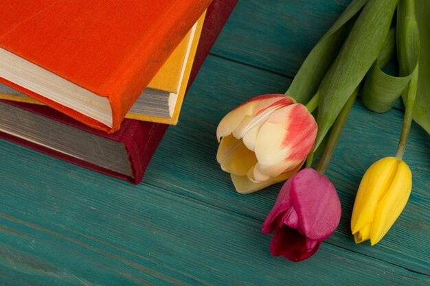 Flores tulipanes y libros sobre una mesa de madera azul.