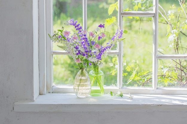 Flores de verano en florero en el alféizar de la ventana en la luz del sol