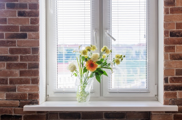 Flores de verano en florero de vidrio en windowsiil