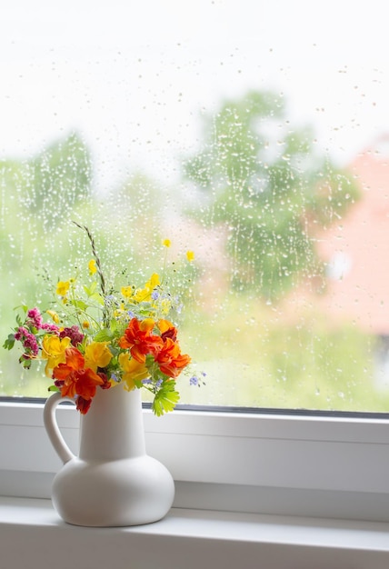 Flores de verano en jarra blanca en el alféizar de la ventana