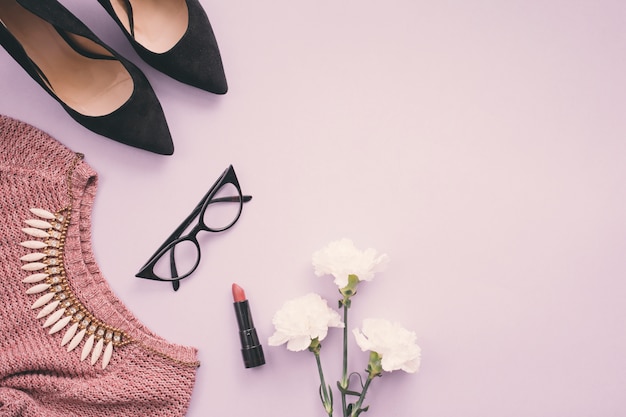 Foto flores con zapatos de mujer, pintalabios, collar y suéter.