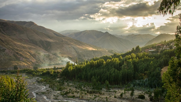 floresta próxima com rio e montanhas distantes, pôr do sol no céu nublado, urcospampa, cusco, peru