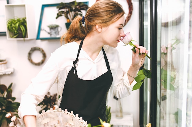 Florist der jungen Frau in einem Blumenladen, der Rose schnüffelt