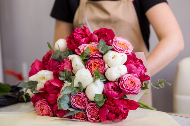 Florist in schwarzen Handschuhen kreiert einen Strauß roter Pfingstrosen