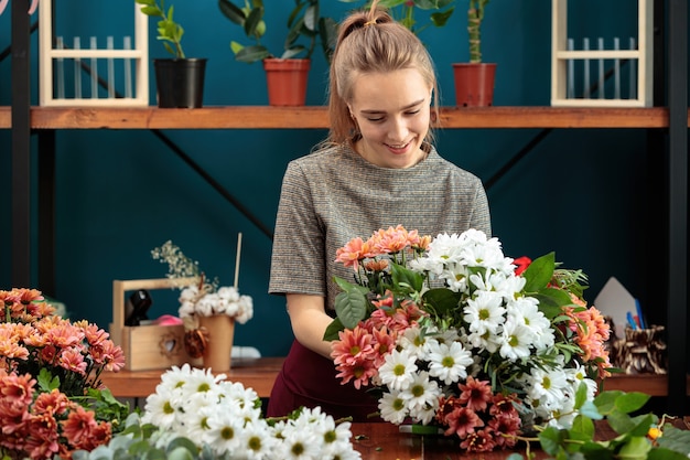 Florist macht einen Strauß aus bunten Chrysanthemen. Ein junges erwachsenes Mädchen arbeitet mit Begeisterung.