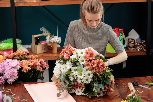 Florist macht einen Strauß bunter Chrysanthemen. Ein junges erwachsenes Mädchen arbeitet mit Begeisterung.