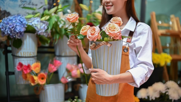 Florista asiática atraente segurando um vaso de rosas organizando sua loja de flores