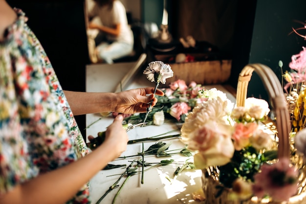 El florista corta un tallo de un clavel y recoge un ramo en la canasta de flores frescas en la florería.