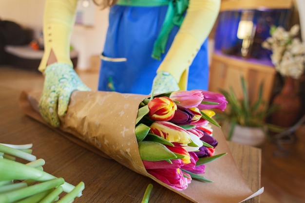 Florista da menina está embalando lindas tulipas em uma loja de flores em papel kraft