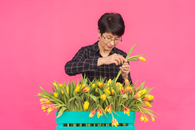 Florista de meia-idade com uma caixa de tulipas de madeira na parede rosa