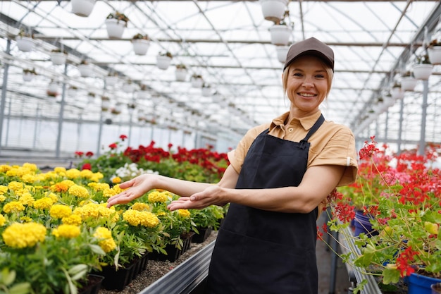 Florista de mulher agradável em uma estufa mostra com as mãos nas flores