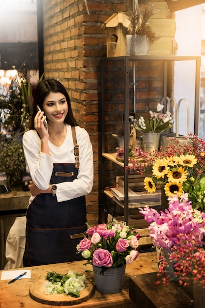 Foto florista de pé em sua loja de flores e usando seu telefone para receber ordens para sua loja