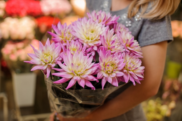 Foto florista em um vestido cinza, segurando um lindo buquê de flores rosa brilhante