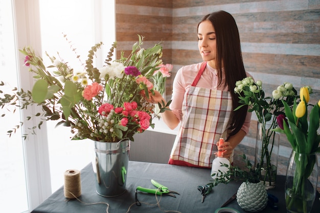 Florista feminina no trabalho: muito jovem morena fazendo moda moderno buquê de flores diferentes. Mulheres que trabalham com flores na oficina