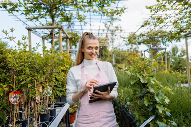 Florista feminina segurando o dono do tablet do centro de jardinagem em pé sorrindo para a câmera foto de alta qualidade