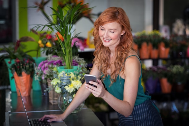 Florista feminina usando telefone celular enquanto estiver usando o laptop