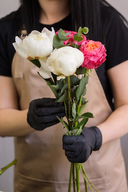 Florista en guantes negros crea un ramo de peonías rojas