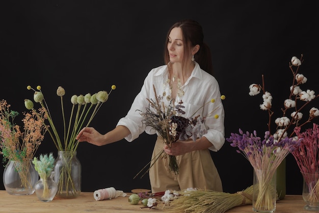 El florista hace un ramo de flores secas en una mesa de madera sobre un fondo oscuro y liso con espacio de copia