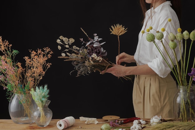 El florista hace un ramo de flores secas en una mesa de madera sobre un fondo oscuro y liso con espacio de copia