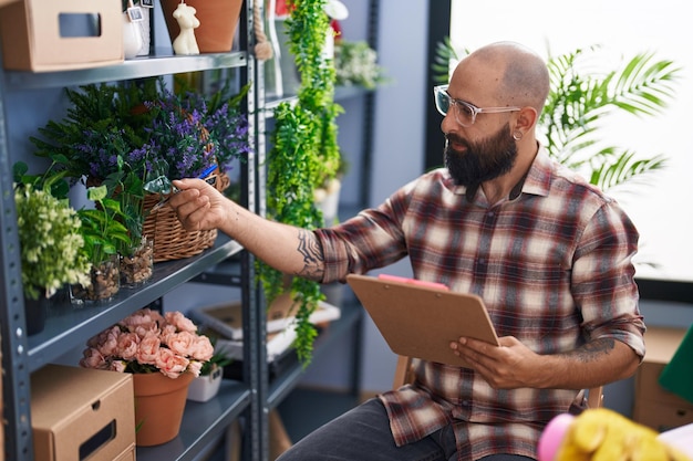 Florista jovem careca lendo documento segurando planta na floricultura