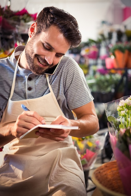 Florista masculina, anotando a ordem no diário enquanto fala no celular