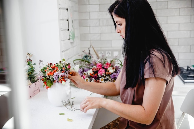 Una florista morena con el pelo largo hace un ramo en un jarrón blanco en la mesa de su estudio