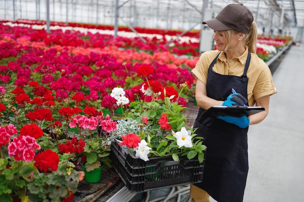 Florista mulher com prancheta em uma estufa com flores coleta um pedido em uma caixa