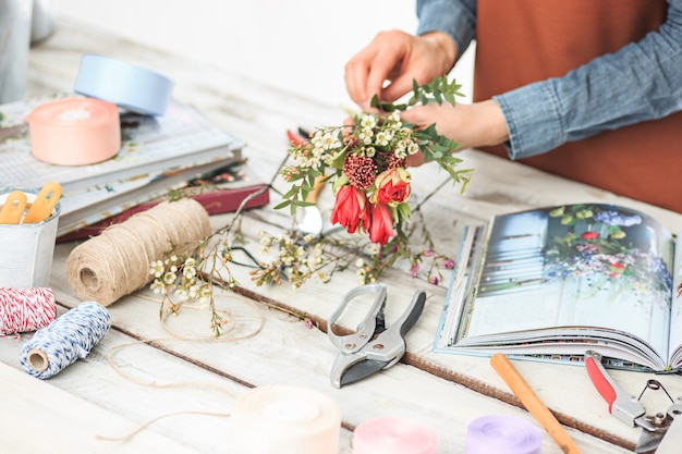 Foto florista no trabalho: as mãos femininas de uma mulher fazendo um buquê moderno de flores diferentes