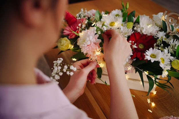 Foto florista no trabalho muito jovem morena fazendo composição moderna de moda de diferentes flores decorando com luzes led em casa