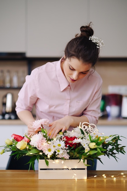 Florista no trabalho muito jovem morena fazendo composição moderna de moda de diferentes flores decorando com luzes led em casa