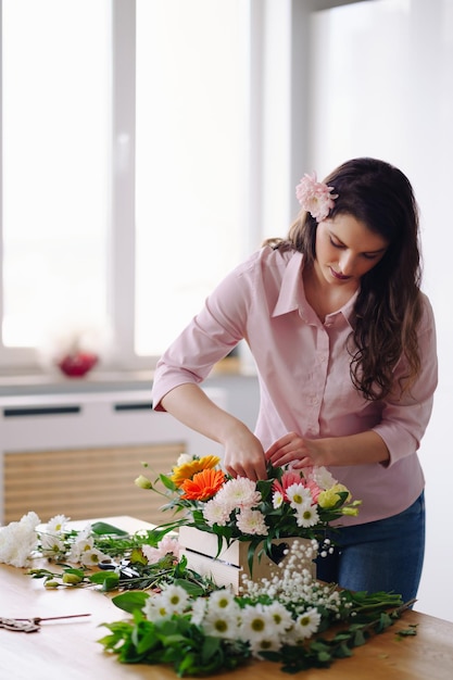 Florista no trabalho muito jovem morena fazendo composição moderna de moda de diferentes flores em casa