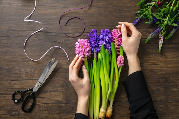 Foto florista no trabalho, mulher fazendo moda buquê moderno de flores diferentes em fundo de madeira