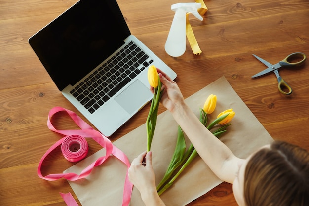 Florista no trabalho: mulher mostra como fazer buquê com tulipas. jovem mulher caucasiana dá workshop online de fazer um presente, um presente para a celebração. trabalhar em casa enquanto conceito isolado, em quarentena.